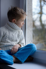 Sad face of a child, 7 years old boy, at home by the window.