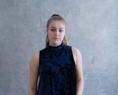 Medium frontal portrait of pretty blond young woman in sleeveless blue velvet dress