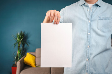 a man in a shirt is holding a white piece of paper at home. realtor concept. house rental agreement. Prepared for your text.