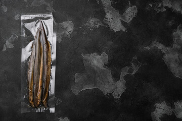 Smoked lamprey vacuum pack, on black dark stone table background, top view flat lay, with copy space for text
