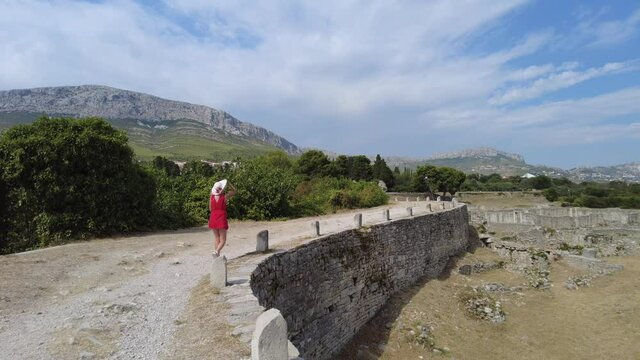 Tourist woman walking in the Salona ruins Ancient Roman city of Dalmatia in Croatia by Caesarea gate. Historic Roman town ruins and City basilica remnants in the Episcopal Center.