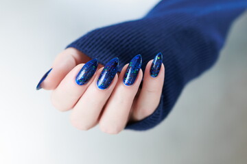 Woman's beautiful hand with long nails and bright blue manicure with bottles of nail polish