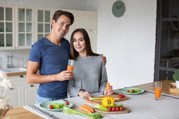 Portrait of happy attractive young loving couple in the kitchen, hugging and cooking together, looking at camera.