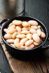 Canned white beans, with metal can, in bowl, on black stone background