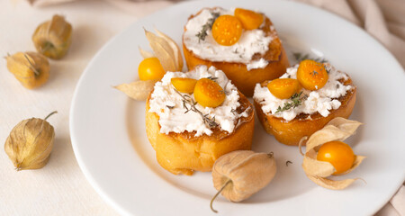 Ricotta bruschetta topped with cape gooseberries on a white plate, copy space. Tropical fruit and food for health concept.