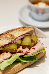 Appetizing sandwich with ham, pickles and herbs on a white table in a cafe. Breakfast and lunch. Vertical. Close-up.