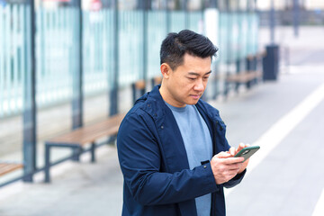Thinking Asian, business man uses phone, near modern office, and airport