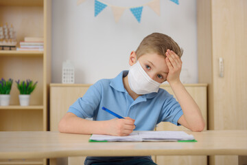 A little boy in a medical mask is learning at home.