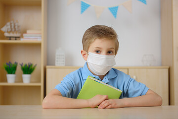 A little boy in a medical mask is learning at home.