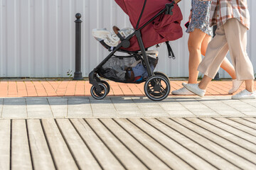 Close-up of the legs of people walking with a stroller on the sidewalk.