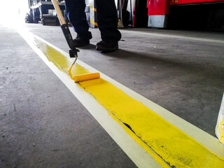 Closeup of a person painting a yellow line on a garage floor under the lights