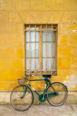 Fototapeta na wymiar Old green bicycle leaning against yellow wall of rural Italian house