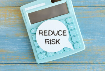 Reduce Risk text on white paper on calculator, wood table background.