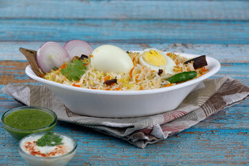 Egg biryani with boiled egg served in an oval white bowl on a wooden table with onion green...