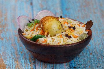 Egg biryani with fried egg in a wooden bowl served on a wooden table with onion