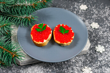 Sandwiches with red caviar on a gray plate on a table with snowflakes and branches of a Christmas tree for a festive New Year's party