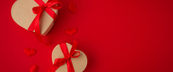 Two wrapped gift boxes in heart shape with red bow ribbon on red background and small padded hearts...