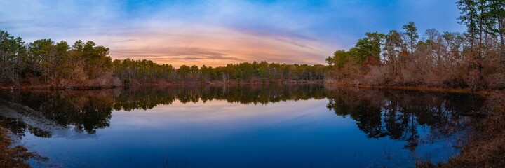 Tranquil panoramic lake and forest landscape at sunset on Cape Cod. Winter blue colors on the sky and water reflections.