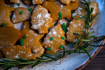 Cookies are on a plate of different shapes, in the foreground there is a cookie in the form of a Christmas tree, decorated with powdered sugar like snow and small green Christmas trees against the