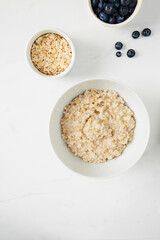 Bowl of porridge, bowl of blueberries and a bowl of oats on white marble countertop