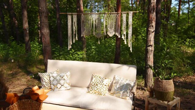 Lounge photo zone with diy sofa and table of cargo pallets in boho style on outdoor wedding ceremony venue in pine forest. Bohemian decor.