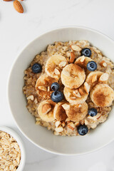 Bowl of porridge topped with banana, blueberries, almonds and cinnamon, a bowl full of oats