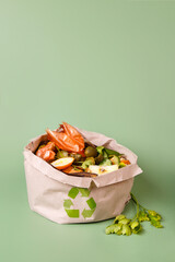 Sorted kitchen waste in paper eco bag on green background. Compost-container. Sustainable life style. Vegetable and fruit peels, scraps from food preparation collected in trash-pack for recycling - 476312557