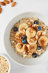 Bowl of porridge topped with banana, blueberries, almonds and cinnamon, a bowl full of oats