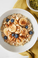 Bowl of porridge topped with banana, blueberries, almonds and cinnamon and a bowl of pumpkin seeds placed on a green linen