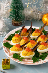 Delicious festive snack - Eggs stuffed with sprats and red caviar on a plate on New year blue background