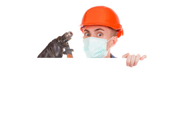 Confident repairman in a protective medical mask, denim jacket and with an orange hard hat on his head holding a drill in his hand on an isolated white background