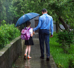 The father leads the child to school in the rain. A manifestation of sacrificial love