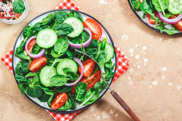 Spring vegetable salad with green spinach, red tomatoes, cucumber, corn salad and onion. Healthy vegan food. Stone kitchen table background. Top view