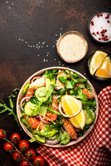 Fresh Salad with chicken, tomatoes, arugula, onion, avocado, sesame seeds and lemon oil dressing. Healthy food. Top view. Brown table