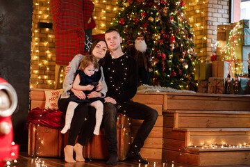 Obraz premium Mother, father with daughter are celebrating Christmas and new year. Parents and little child having fun near Christmas tree indoors. The morning before Xmas.