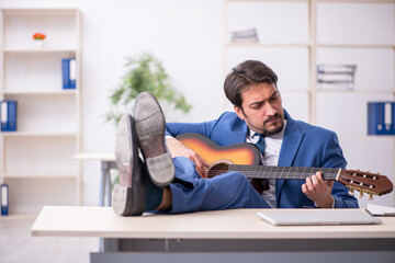 Young male employee playing guitar at workplace