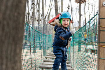Portrait happy brave courage little toddler child boy wear safety equipment helmet enjoy passing obstacle course forest rope adventure park on cold winter day. Active outside leisure amusement camp