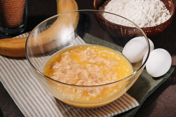 A mix of mashed banana and melted butter in a glass bowl and ingredients for cooking banana bread