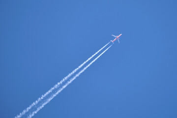Distant passenger jet plane flying on high altitude on clear blue sky leaving white smoke trace of...