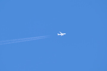 Distant passenger jet plane flying on high altitude on clear blue sky leaving white smoke trace of contrail behind. Air transportation concept