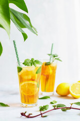 Iced iced tea in a glass with a straw, mint leaf and lemon slices inside. Cool drinks in the heat. Vertically photo