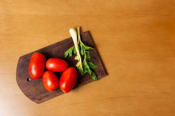Tomates y apios de huerta orgánica en vista cenital sobre tabla y mesa de madera