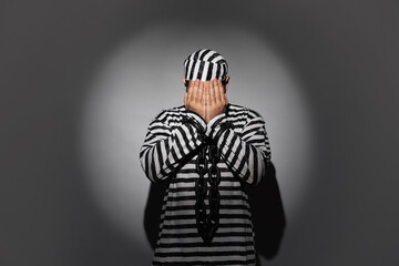 Prisoner in special uniform with chained hands on grey background
