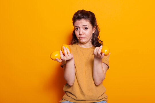 Smiling person holding yellow citrus fruits on camera in studio. Young woman showing fresh raw natural lemons for snack with vitamins. Adult with organic colorful fruit for vegetarian diet