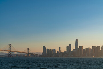 A picturesque view of The Bay Bridge and San Francisco Skyline Panorama at sunset golden hour from Treasure Island, California, United States. Cityscape with mist and foggy air.