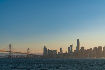 Fototapeta na wymiar A picturesque view of The Bay Bridge and San Francisco Skyline Panorama at sunset golden hour from Treasure Island, California, United States. Cityscape with mist and foggy air.