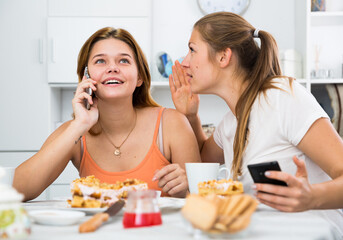 Girl is playfull talking by phone and her girlfriend is interesting it at home.
