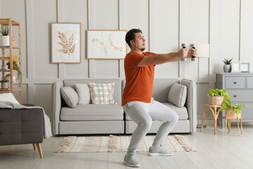 Overweight man doing squat exercise with dumbbells at home