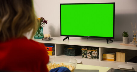 Fototapeta na wymiar Green Screen TV Close up. Shot behind model Shoulder watching Tv sitting on the couch.