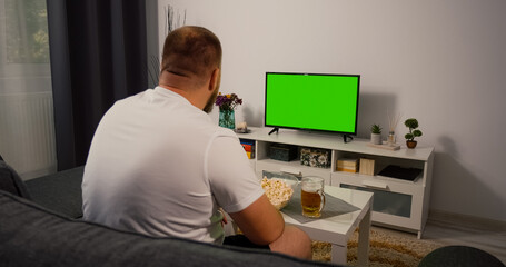 Man watches Green Screen Chroma Key Screen. Watching Tv at home interior. Watching a sport match.